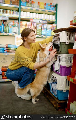 Cheerful young woman customer with dog at pet shop choosing new carrier for transportation during adventure and trip. Cheerful young woman customer with dog at pet shop new choosing carrier