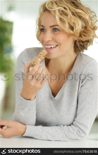 cheerful young woman eating diet cereal bar