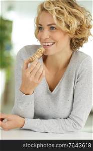 cheerful young woman eating diet cereal bar
