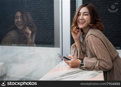 cheerful young woman holding smartphone at window