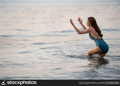 cheerful young woman in swimsuit playing water splashing on the sea beach at Koh Chang island, Thailand