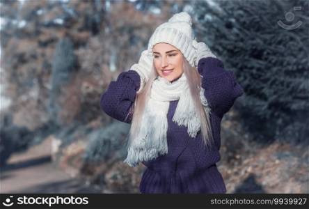 Cheerful young woman in warm clothing, winter day outdoors. Half length of happy girl wearing wool cap, scarf and sweater. Female person in cold weather.