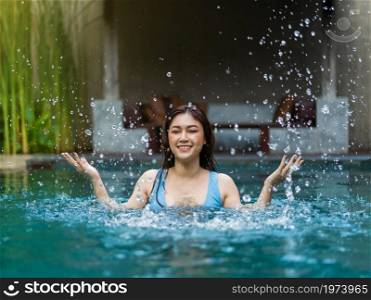 cheerful young woman playing water splashing in the swimming pool