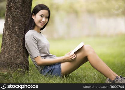 Cheerful young woman reading books on the lawn