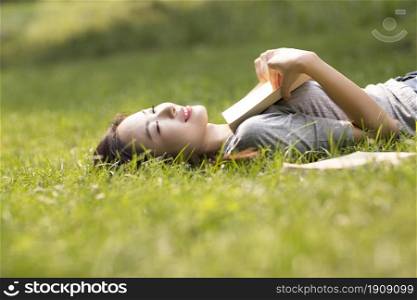 Cheerful young woman reading books on the lawn