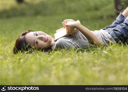 Cheerful young woman reading books on the lawn