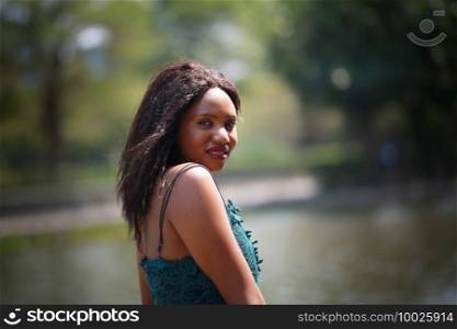 Cheerful young woman standing outdoor against water park in the garden.. Portrait of afro American women posing at outdoor.
