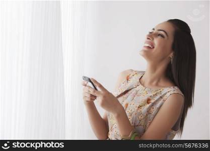 Cheerful young woman text messaging by curtains