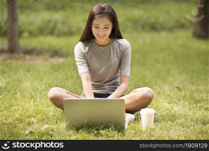 Cheerful young woman using her laptop on the lawn