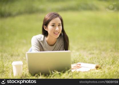 Cheerful young woman using her laptop on the lawn