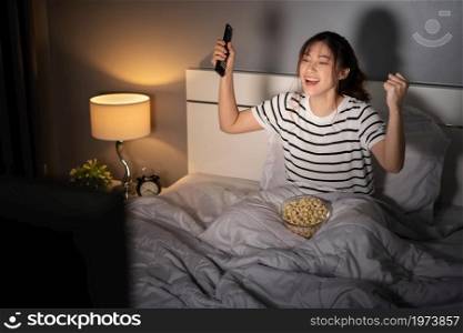 cheerful young woman watching sport TV with arm raised on a bed at night