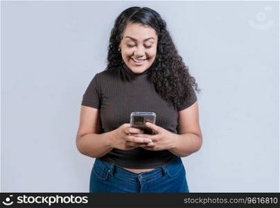 Cheerful young woman with curly hair texting on cell phone isolated. Smiling latin girl using cell phone isolated