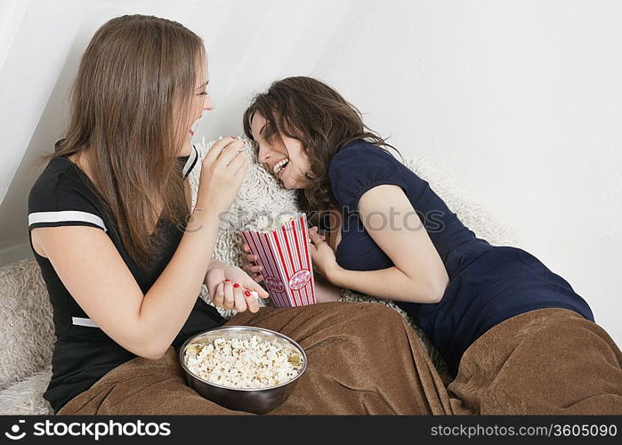 Cheerful young women eating popcorn in bed