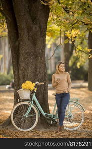 Cheerfull young woman with bicycle using smartphone in autumn park