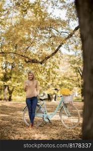 Cheerfull young woman with bicycle using smartphone in autumn park