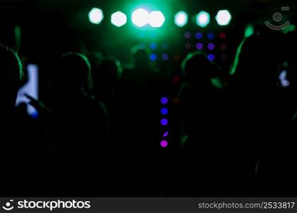 cheering crowd in front of bright blue green stage lights. Silhouette image of people dance in disco night club or concert at a music festival. cheering crowd in front of bright blue green stage lights. Silhouette image of people dance in disco night club or concert at a music festival.