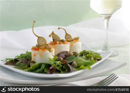 Cheese and capers sweet and sour sauce and pistachios in the green leaves with a glass of white wine
