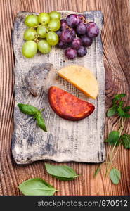 Cheese and grapes decorated with basil leaves on handmade pottery plate on old wooden table from above