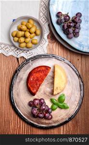 Cheese black grapes and olives decorated with mint on handmade pottery plates on old wooden table from above