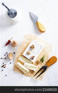Cheese, herbs, nuts and knife on white table. Overhead view. Selective fucus.