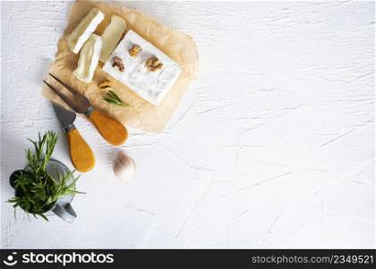 Cheese, herbs, nuts and knife on white table. Overhead view. Selective fucus.