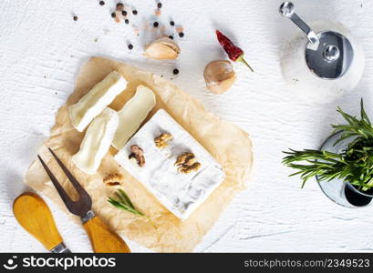 Cheese, herbs, nuts and knife on white table. Overhead view. Selective fucus.