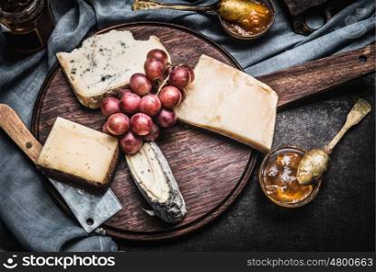 Cheese on rustic wooden Plate with knife, spoon and sauces, top view. Dark style
