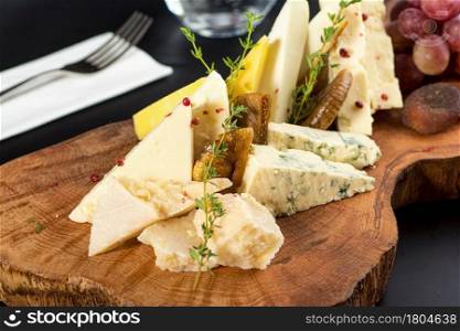 Cheese plate served with grapes, jam, figs, crackers and walnuts on a dark stone background
