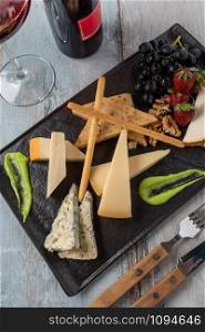 Cheese plate served with grapes, strawberry, crackers and nuts on a wooden background. Gourmet cheese plate