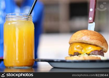 Cheeseburger and lemonade in jar on table, woman in background eating another one