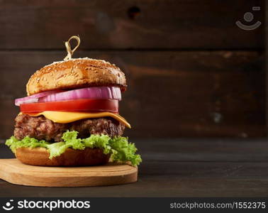 cheeseburger with tomatoes, onions, barbecue cutlet and sesame bun on an old wooden cutting board, brown background. Fast food, copy space