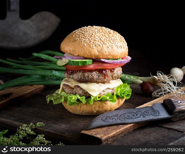 cheeseburger with vegetables on a brown old wooden board, black background