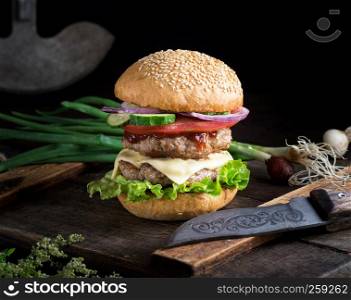 cheeseburger with vegetables on a brown old wooden board, black background