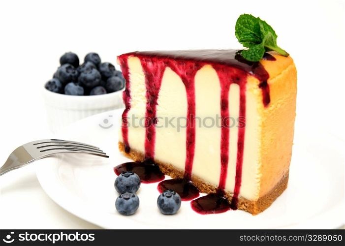 Cheesecake And Blueberries. Plain Cheesecake with a Blueberry sauce poured over the top with fresh berries on the plate next to the cake and topped with a mint leaf.