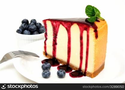 Cheesecake And Blueberries. Plain Cheesecake with a Blueberry sauce poured over the top with fresh berries on the plate next to the cake and topped with a mint leaf.