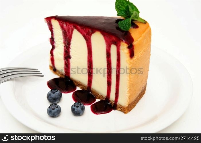 Cheesecake. Plain Cheesecake with a Blueberry sauce poured over the top with fresh berries on the plate next to the cake and topped with a mint leaf.