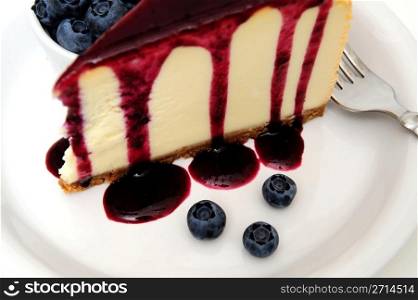 Cheesecake With Blueberry Sauce. Plain Cheesecake with a Blueberry sauce poured over the top with fresh berries on the plate next to the cake and topped with a mint leaf.