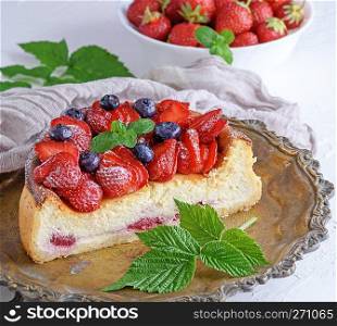 Cheesecake with ripe fresh strawberries on a copper round plate, close up