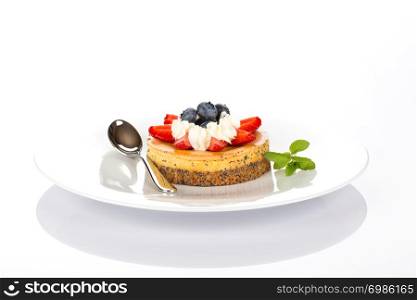 Cheesecake with strawberries, blueberries, mint and cream on white plate.
