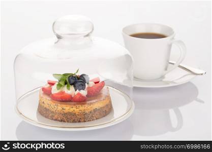 Cheesecake with strawberry, blueberry, mint and cream under glass bell and cup of coffee.
