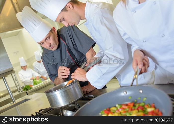 Chef checking trainee&rsquo;s pan of food