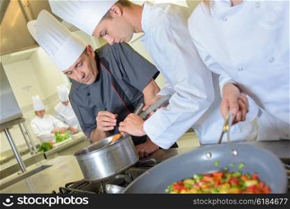 Chef checking trainee&rsquo;s pan of food