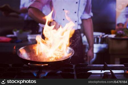 Chef cooking and doing flambe on food in restaurant kitchen. Chef doing flambe on food