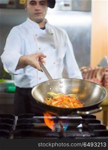 Chef cooking and doing flambe on food in restaurant kitchen. Chef doing flambe on food