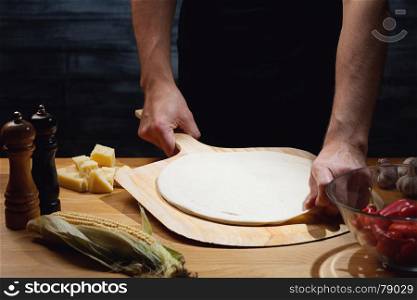 Chef cooking pizza, putting blank pizza base on board. Low key shot, close up of hands, some ingredients around on table.
