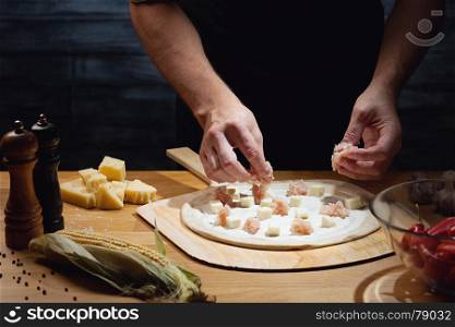 Chef cooking pizza, putting topping on pizza base. Low key shot, close up of hands, some ingredients around on table.