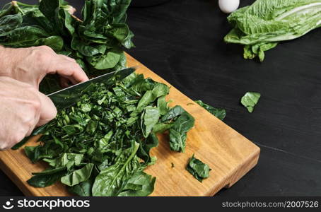 Chef cuts juicy spinach leaves on a wooden cutting board. Organic and healthy food. The idea of making a salad or omelet for breakfast