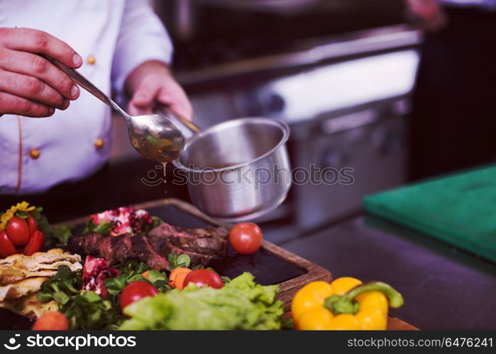 Chef hand finishing steak meat plate with Finally dish dressing and almost ready to serve at the table. Chef hand finishing steak meat plate