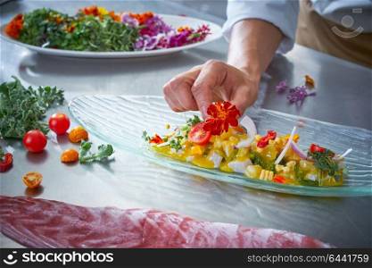 Chef hands garnishing flower in ceviche dish at stainless steel kitchen