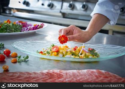 Chef hands garnishing flower in ceviche dish at stainless steel kitchen